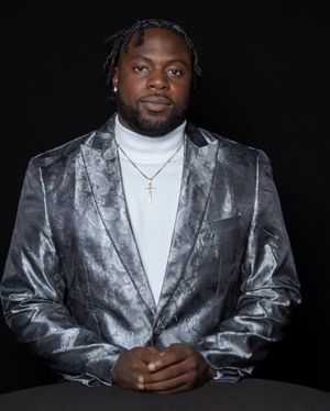 Professional studio portrait of someone wearing a silver metallic blazer and white shirt against a black background.
