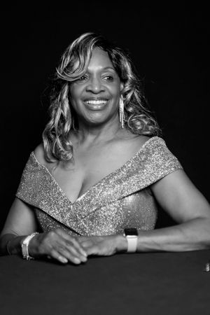 Black and white studio portrait of a woman wearing a sparkly off-shoulder gown and elegant jewelry.