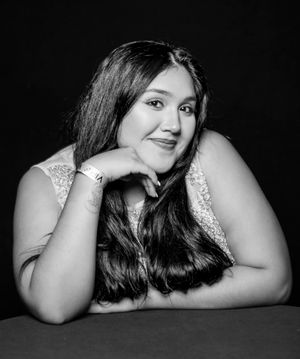 Woman in sparkly dress resting head on hand in artistic black and white portrait.