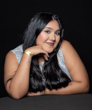 Woman in sequined dress poses elegantly against dark background.