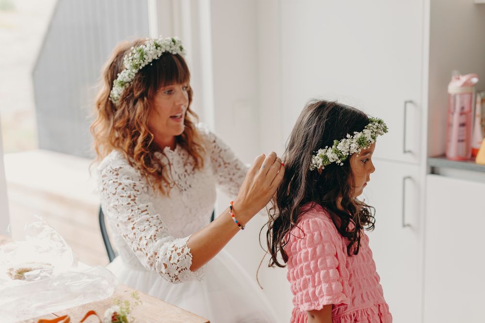 Two people wearing delicate floral crowns and dresses share an intimate styling moment in soft natural light.