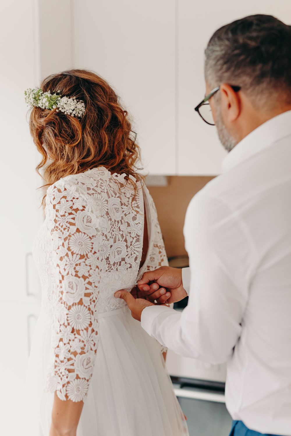 A bride in a white lace dress gets help with final adjustments before her wedding ceremony.