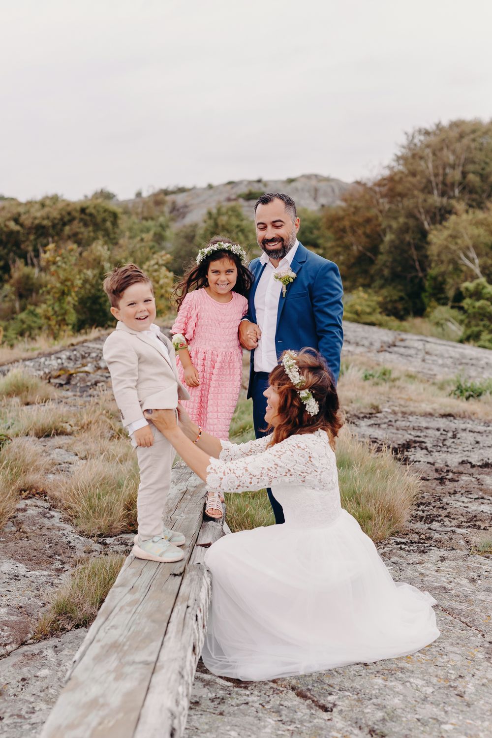 A joyful wedding party plays and dances together on a rocky hillside path during an autumn day.