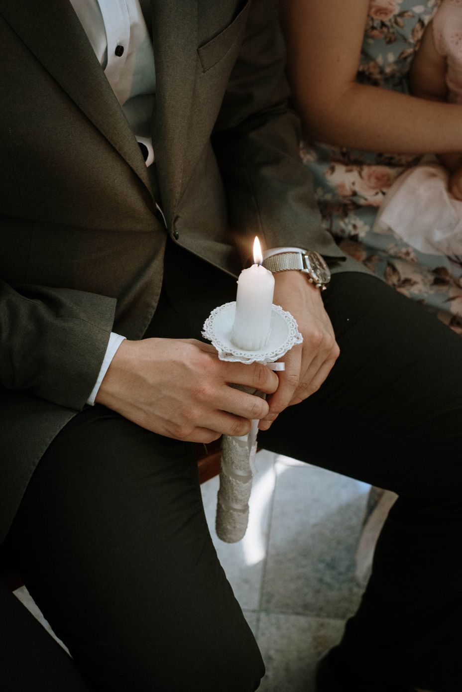 Close-up of hands in formal attire holding a lit white taper candle during a wedding ceremony.