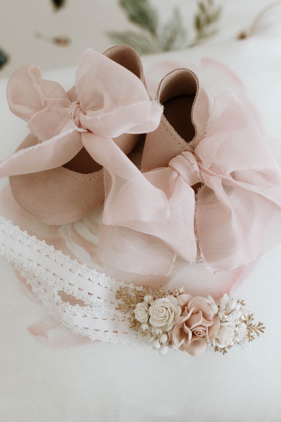 Delicate pink ballet shoes with satin ribbons and floral embellishments arranged in a soft, romantic composition.