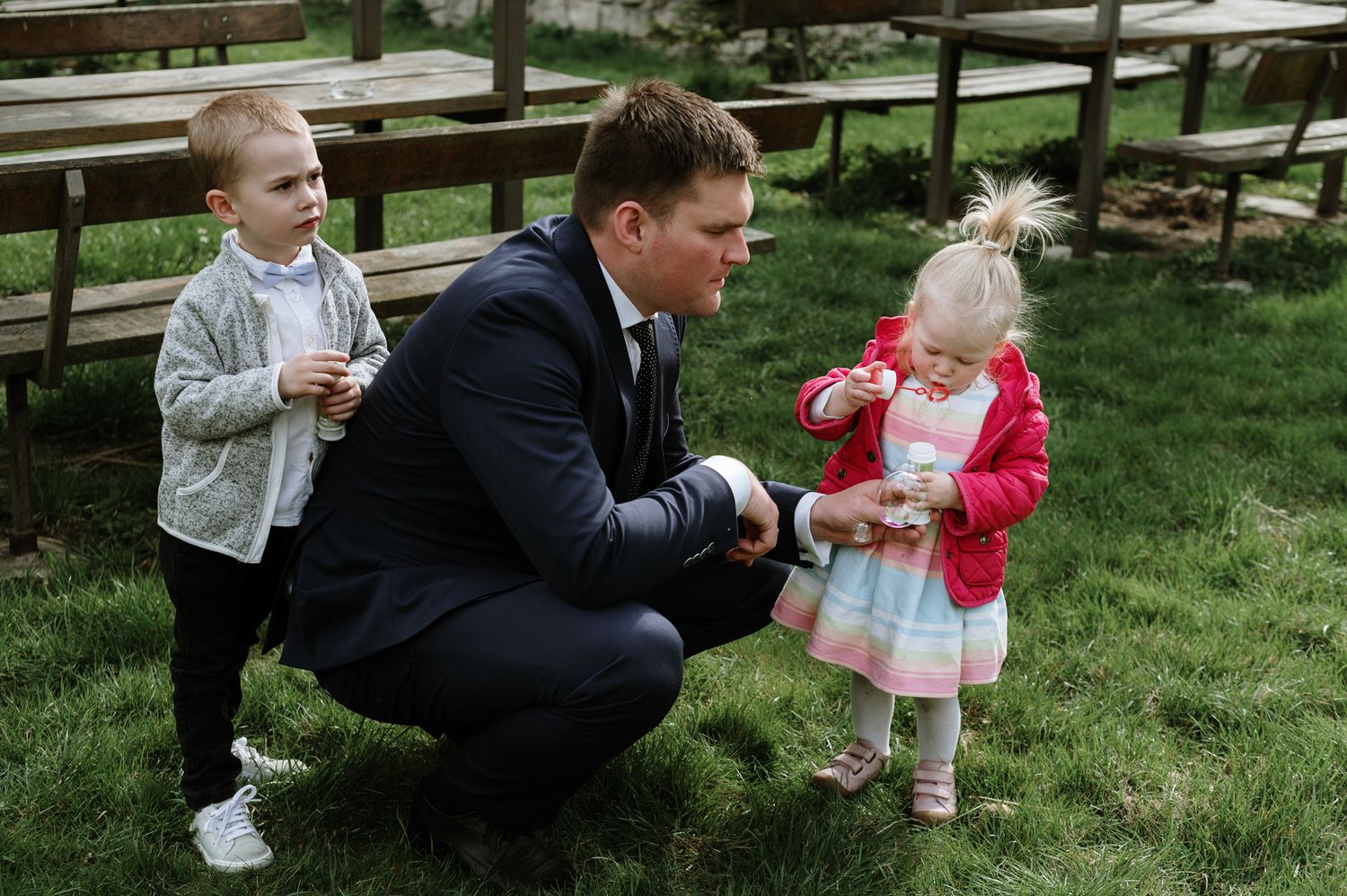 A sequence of candid outdoor moments showing playful interactions between adults and a small child on grass.