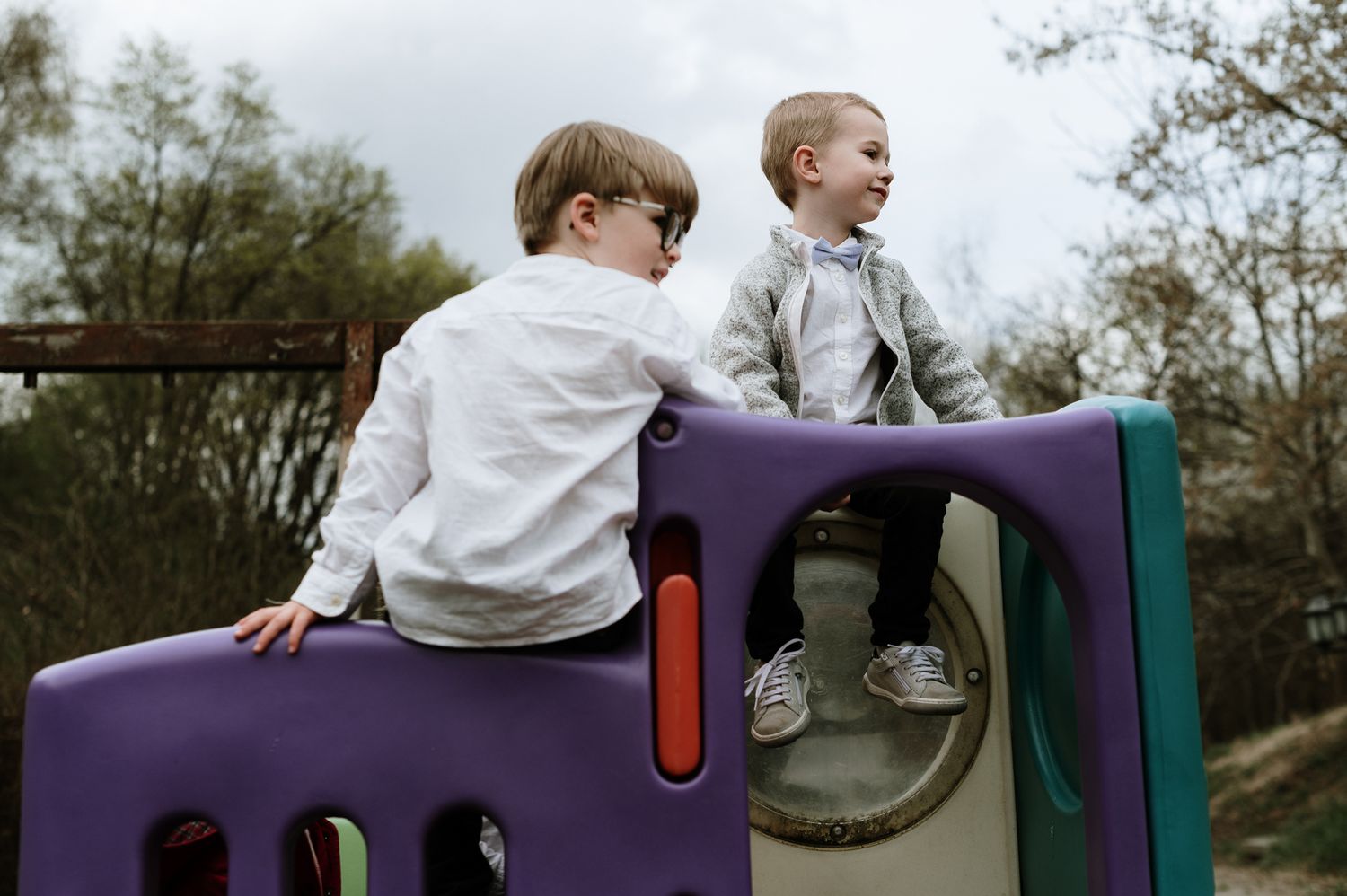 Two young children play and laugh together on colorful playground equipment at an outdoor park.