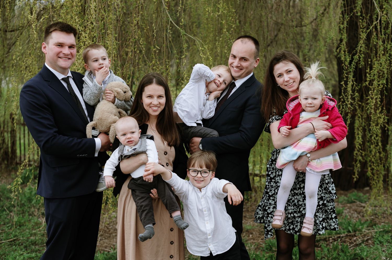 Family group photos taken outdoors under weeping willow trees during a formal occasion.