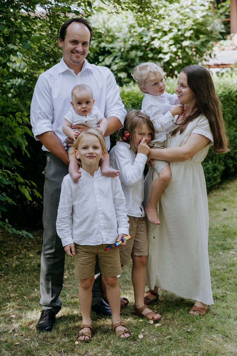 A family wearing coordinated white and beige outfits poses together on green grass during a summer photoshoot.