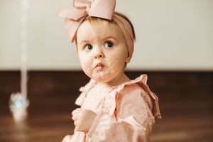 Close-up of baby girl with pink bow headband and cake smash frosting on her face at first birthday.
