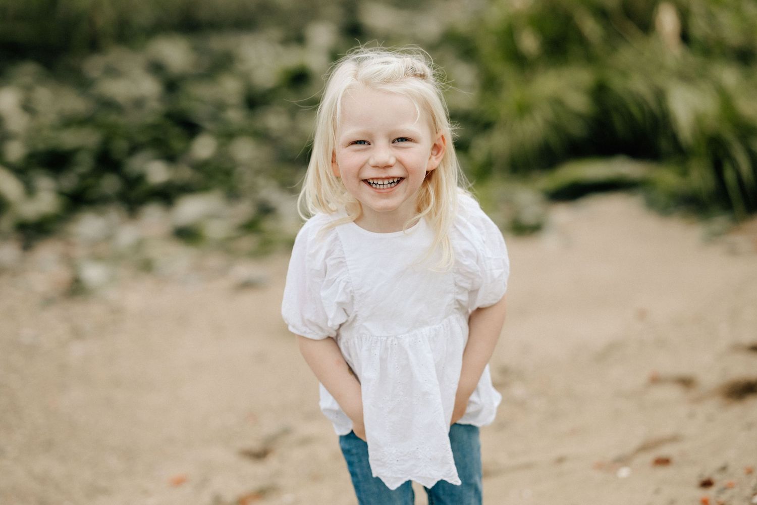 A person in a white lace dress and blue jeans runs joyfully through a natural outdoor setting.