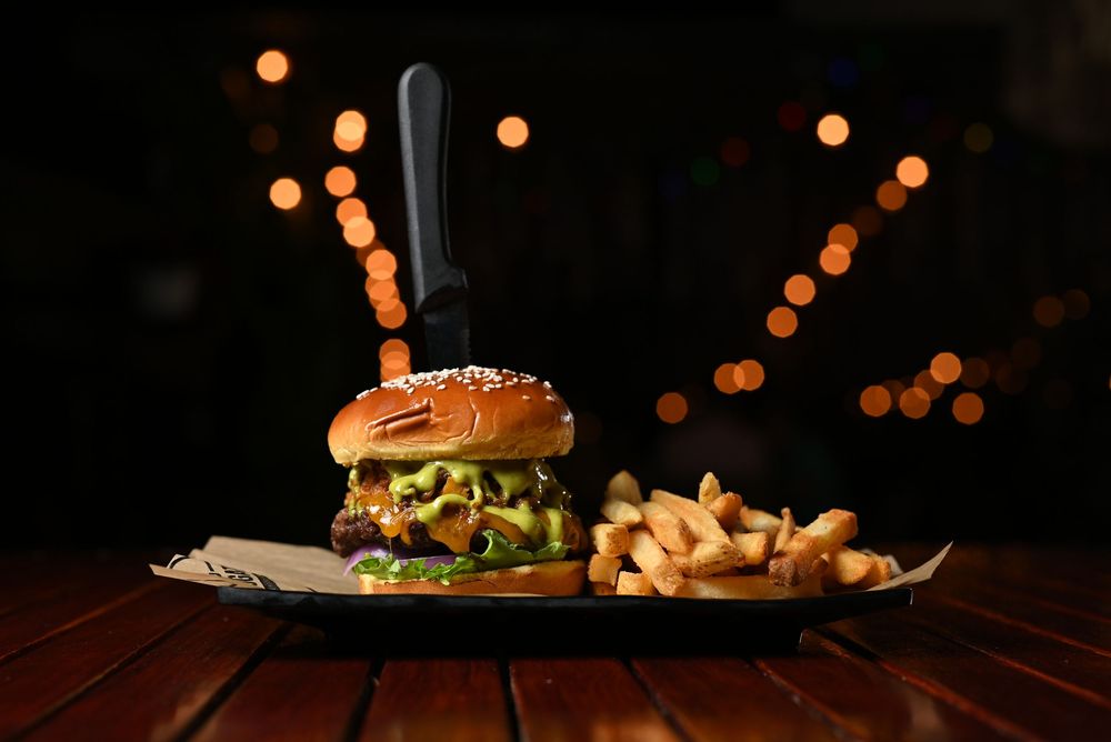 Juicy cheeseburger with golden french fries on dark wooden table with glowing bokeh lights in background.