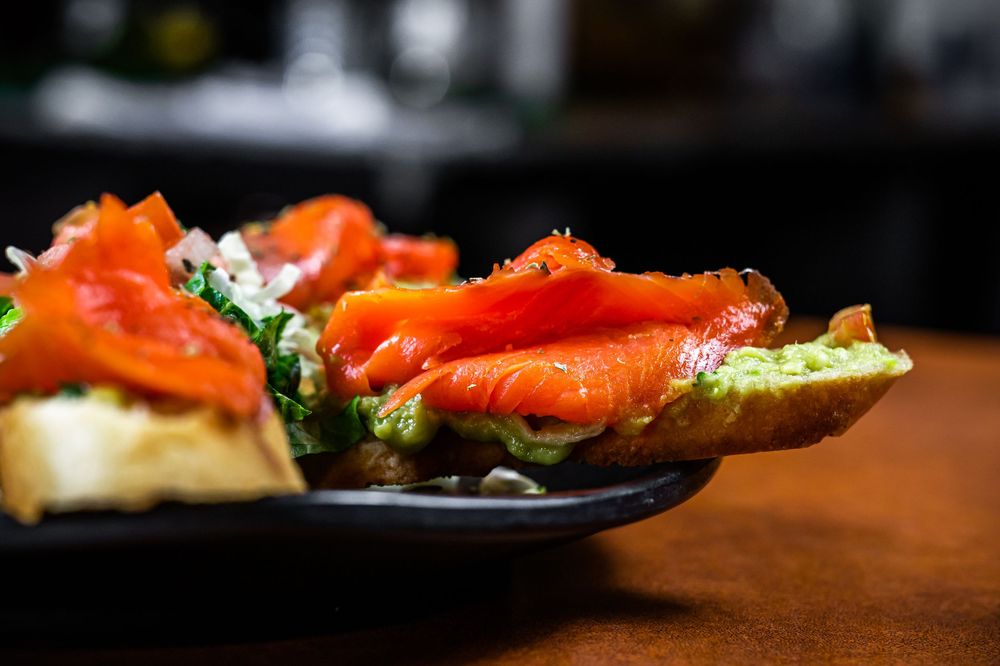 Fresh salmon slices arranged on a dark plate with garnish and herbs in a fine dining presentation.