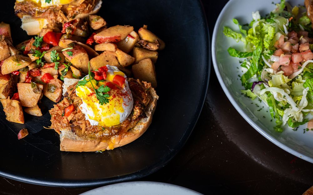 Gourmet brunch dishes including eggs, salads, and sandwiches arranged on dark plates.