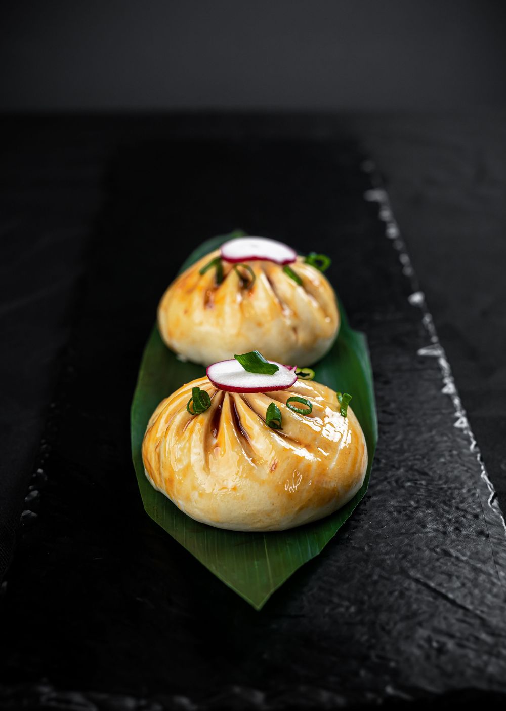 Golden steamed dumplings served on green banana leaves against a dark slate background.