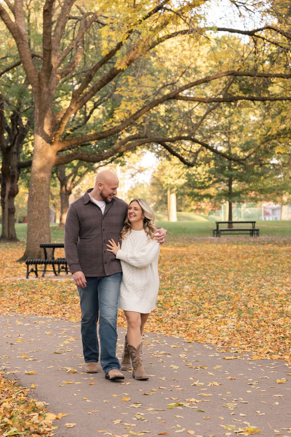 A couple walking together on a path covered in autumn leaves while enjoying a romantic fall day in the park.