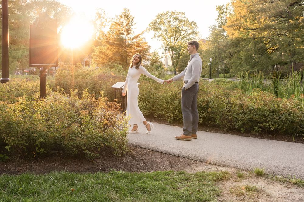 A couple walks hand in hand on a sunlit path through a lush garden during golden hour sunset.