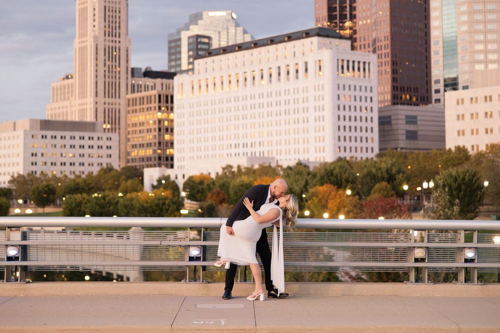 A romantic couple embraces on a rooftop with the Minneapolis skyline and autumn trees in the background.