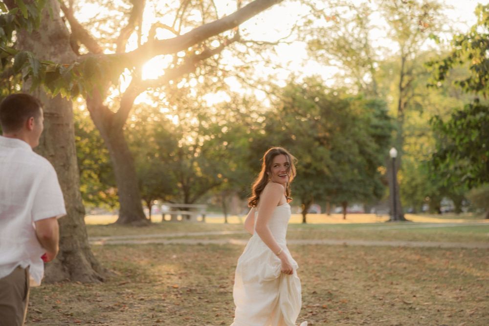 A couple shares a romantic moment in a sunlit park during golden hour as the bride looks back with joy.
