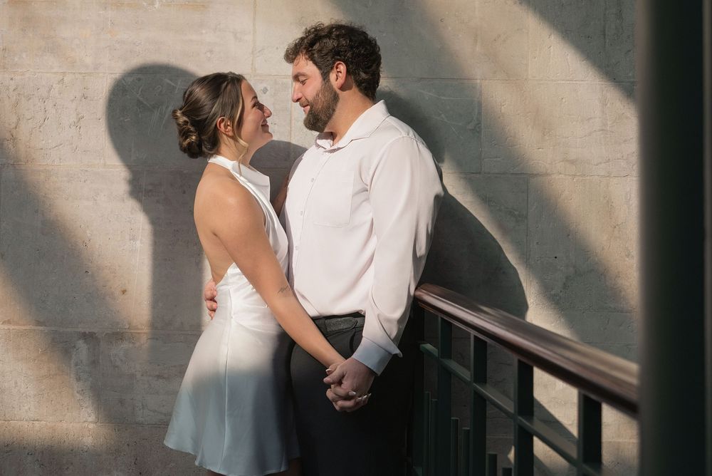 A romantic couple in white outfits dance together against a wall with dramatic shadows.