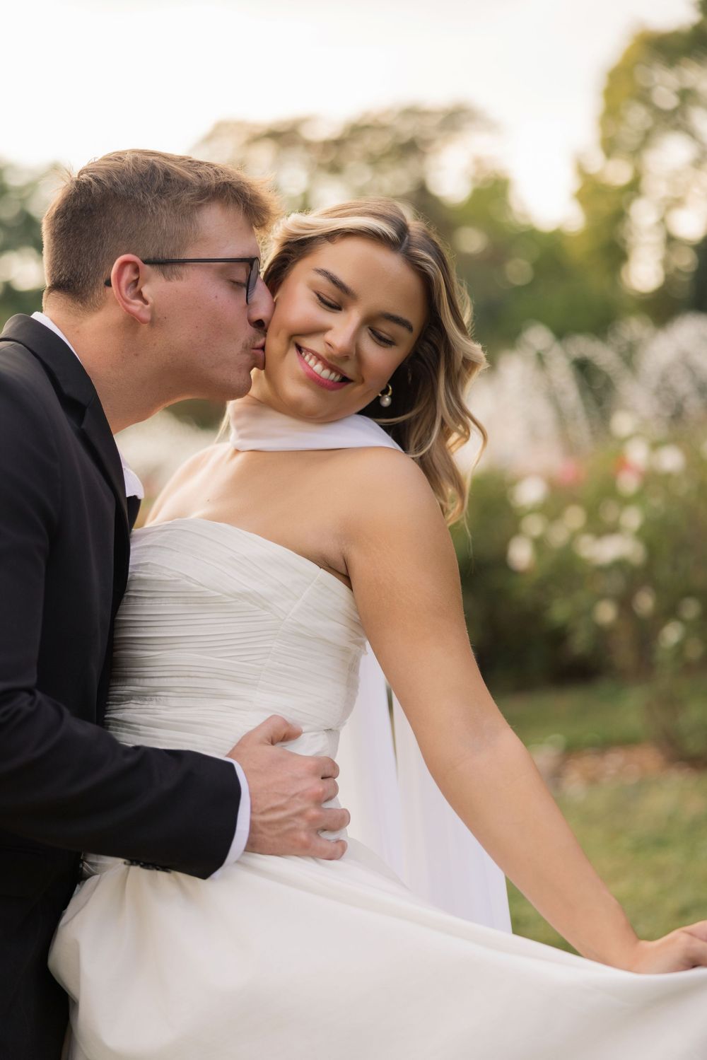 A romantic wedding couple embraces outdoors in soft natural lighting during their photo session.