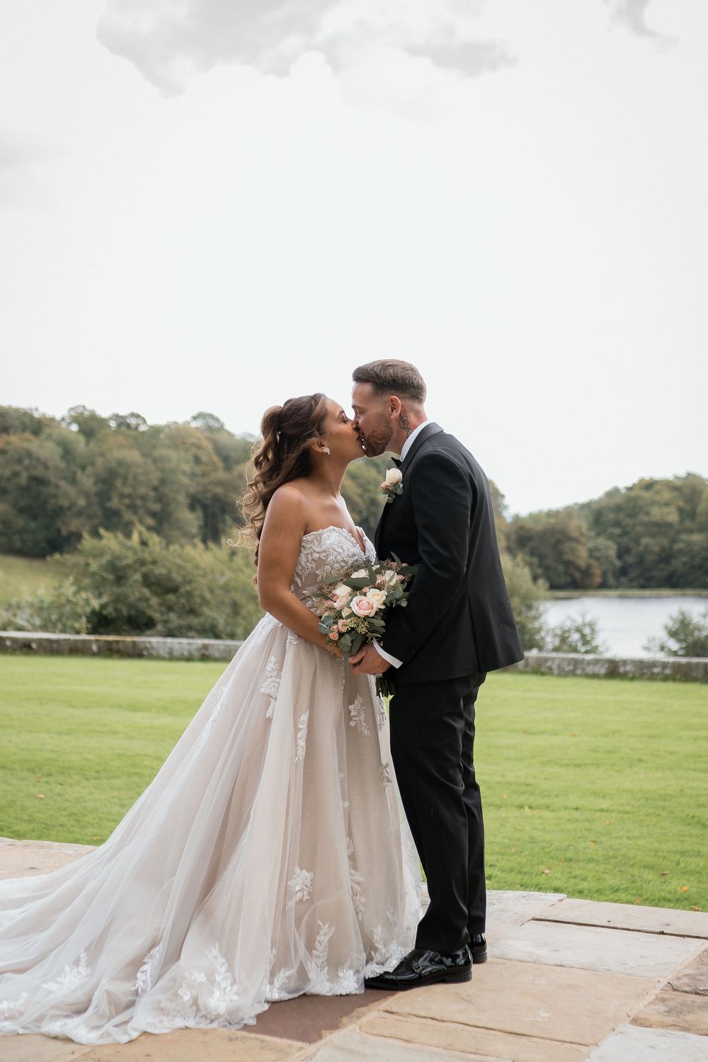 A romantic wedding couple shares intimate moments on a scenic lakeside patio during their special day.