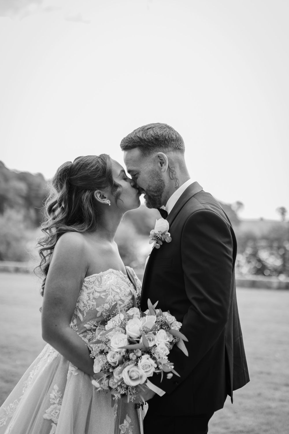 Black and white wedding photo of a couple sharing an intimate moment with a beautiful bouquet of roses.