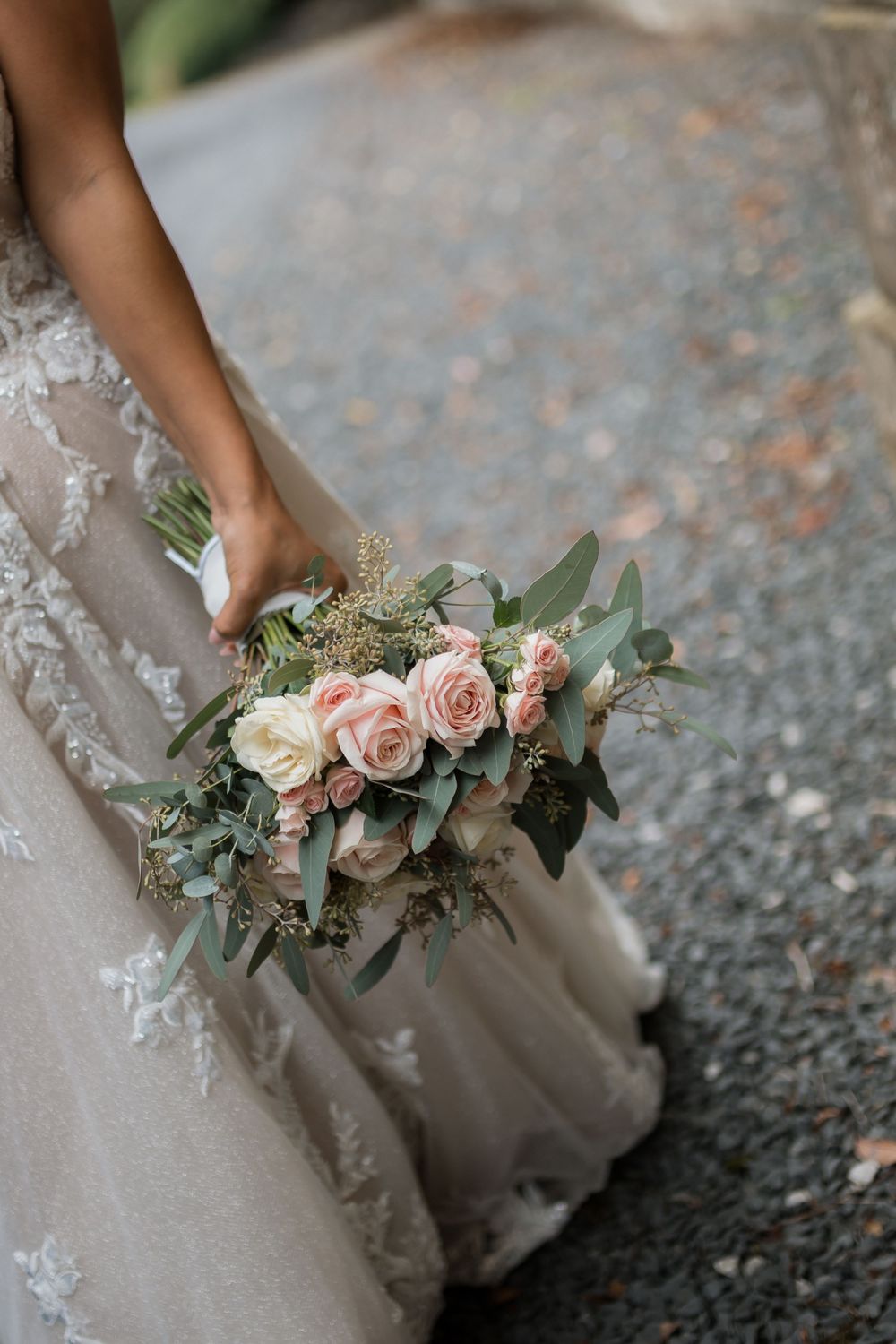 Close-up view of a delicate bridal bouquet featuring blush pink roses and eucalyptus against a lace wedding dress.