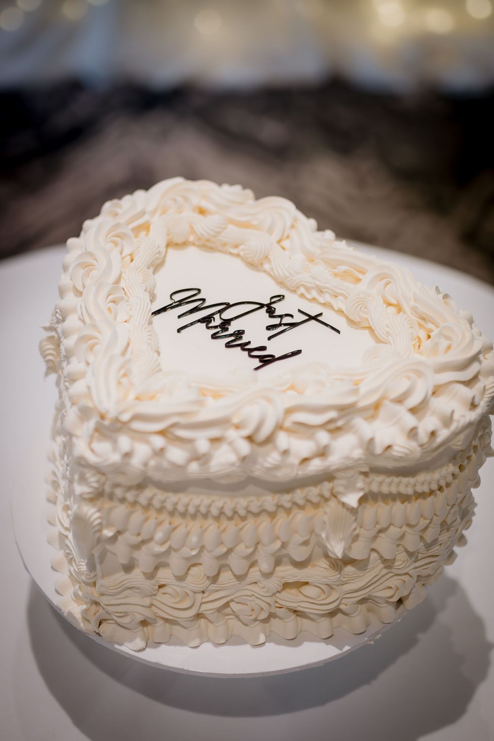 Heart-shaped white wedding cake with delicate piped frosting details and elegant script writing on top.