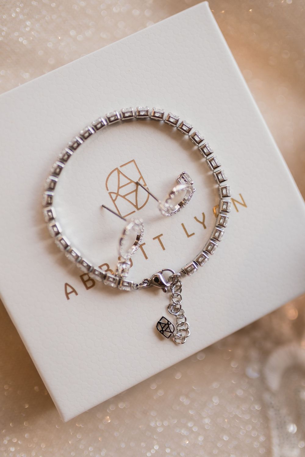 A delicate silver bracelet with crystal accents rests on a white jewelry box with gold lettering.