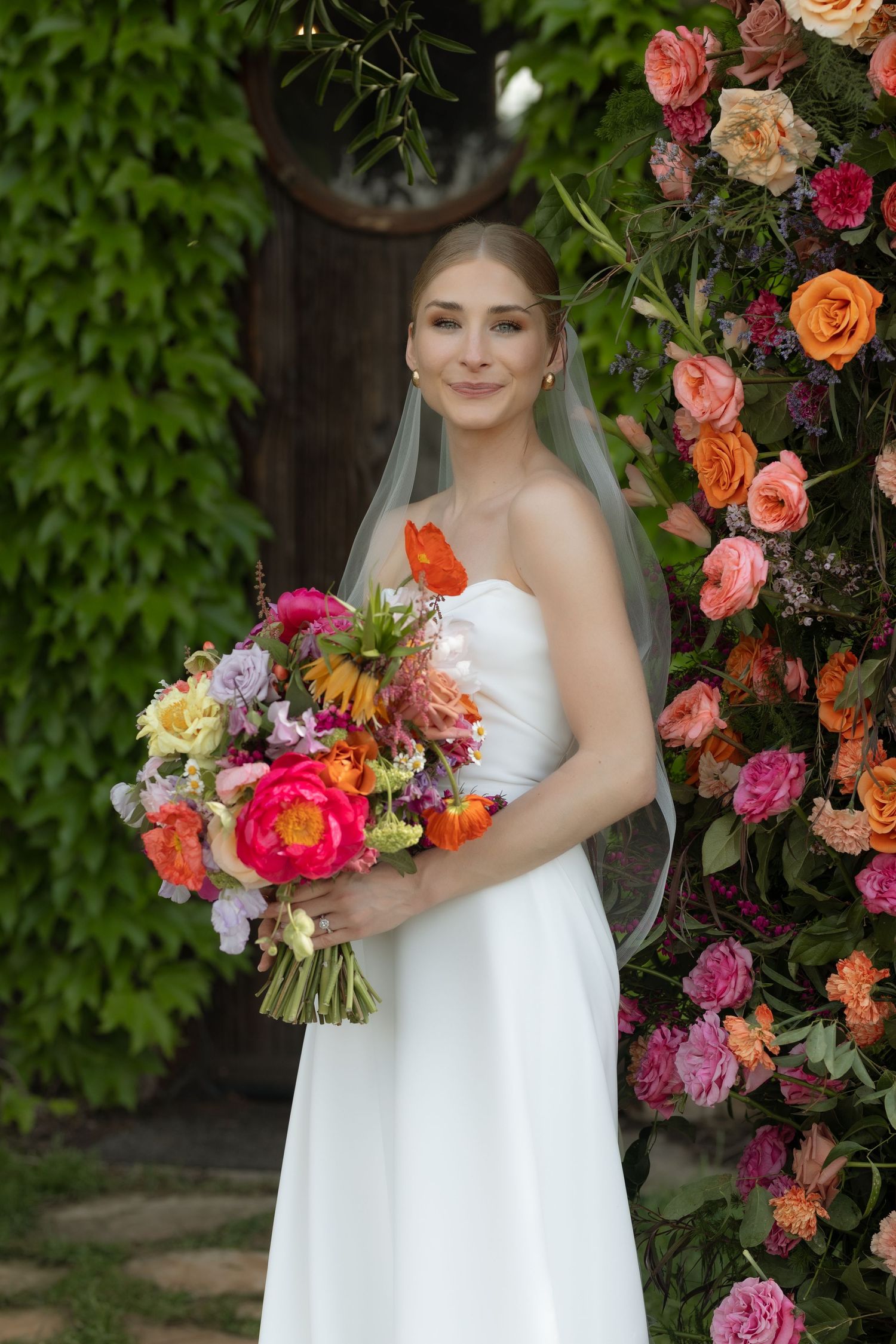 A wedding couple dances and embraces in front of elegant white chairs and colorful floral arrangements at their reception.