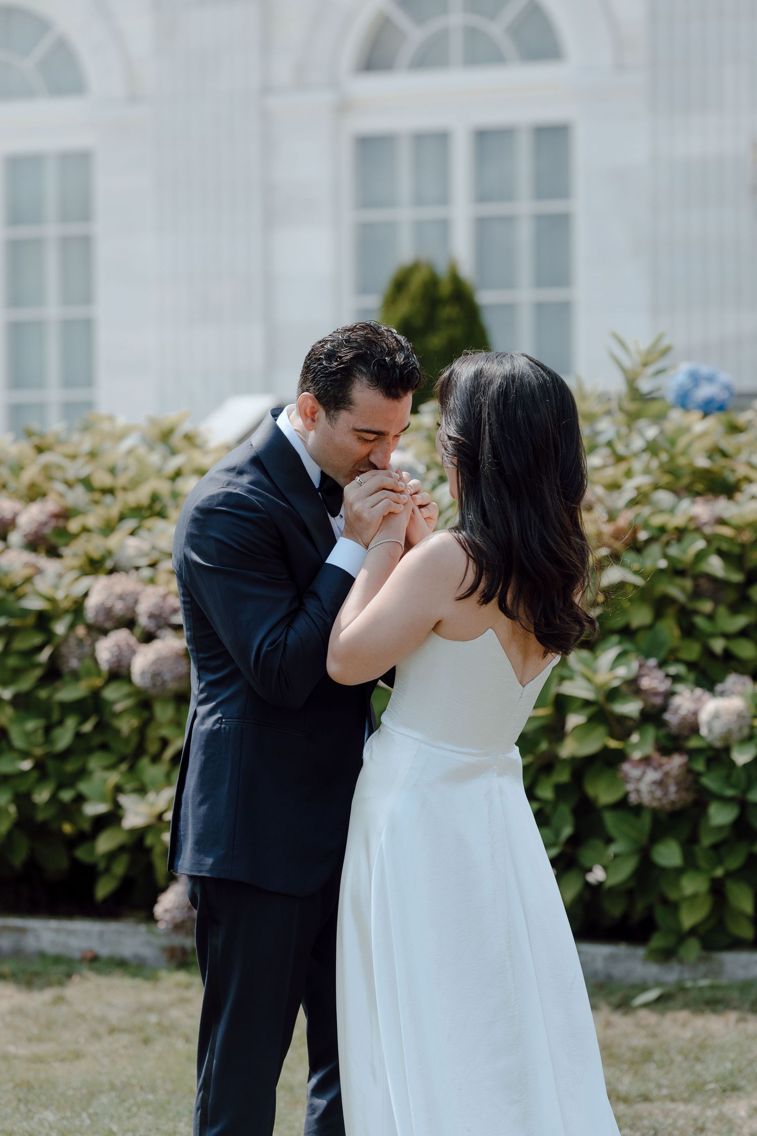 A romantic wedding couple shares intimate kisses in front of blooming hydrangea bushes on their special day.