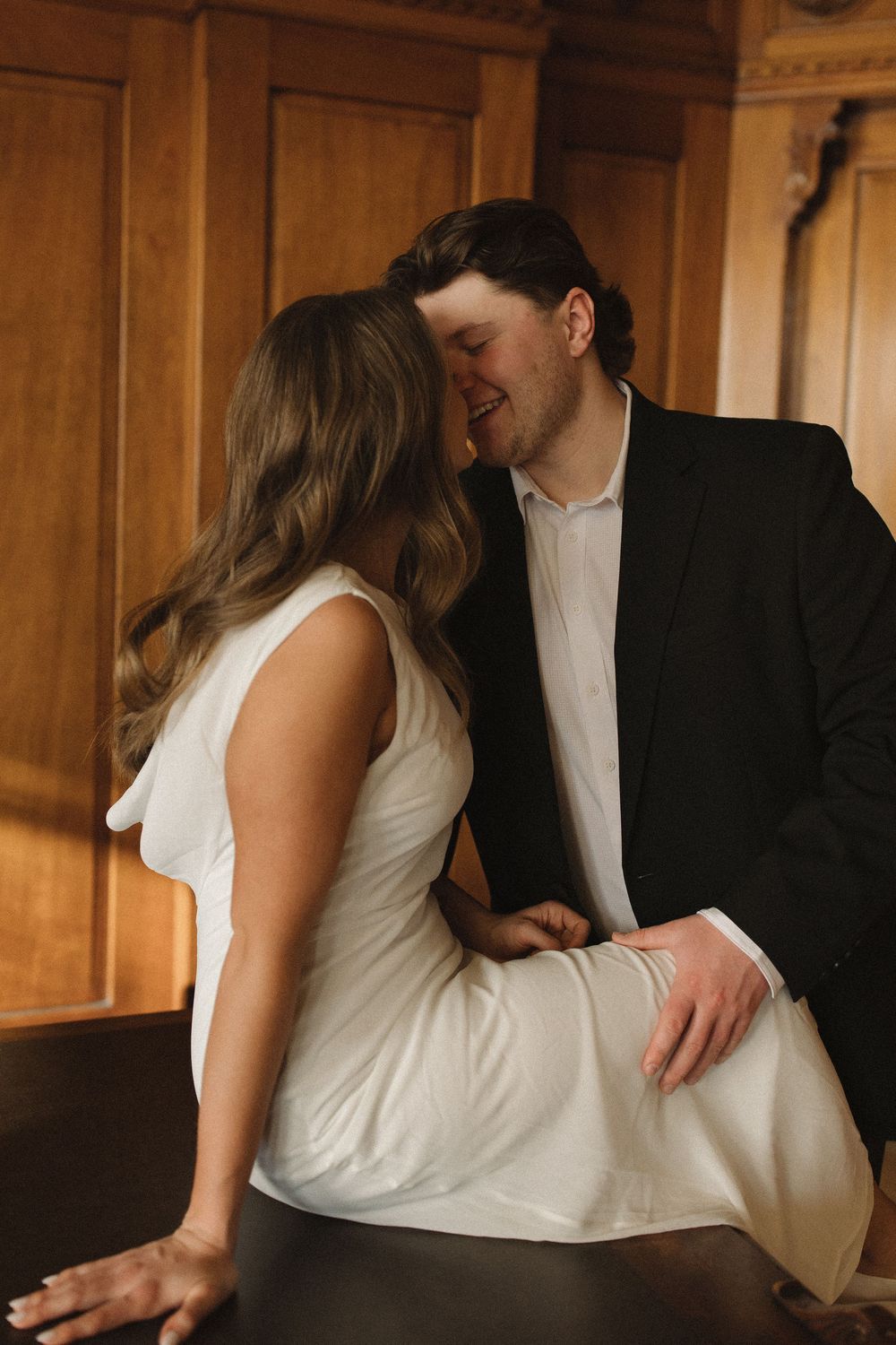 A romantic couple embraces in an intimate moment against a warm wooden interior backdrop.