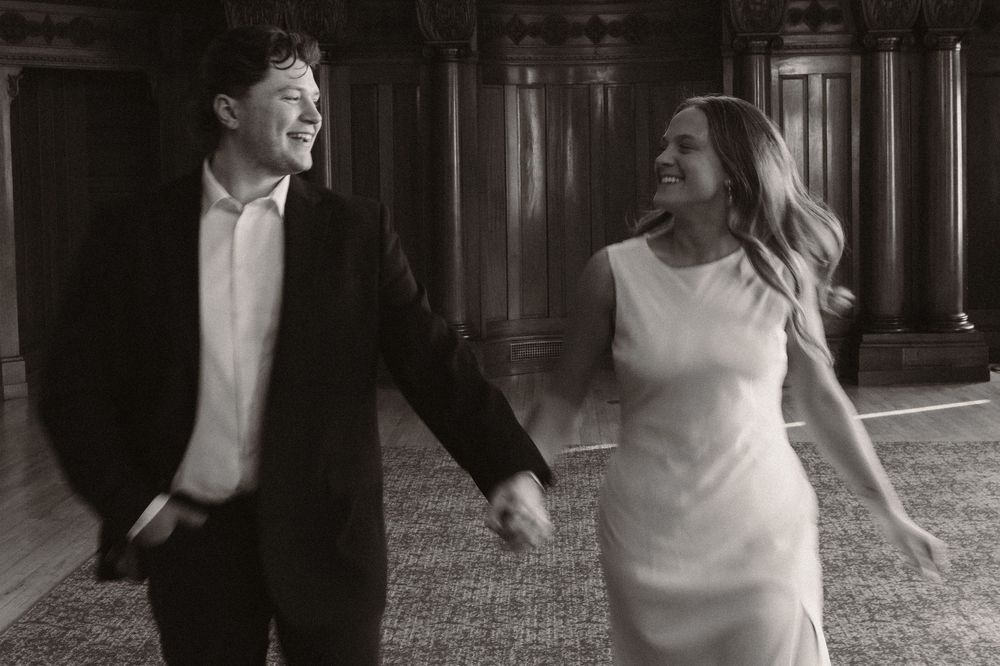 A joyful black and white moment captured of a couple laughing and running together indoors.