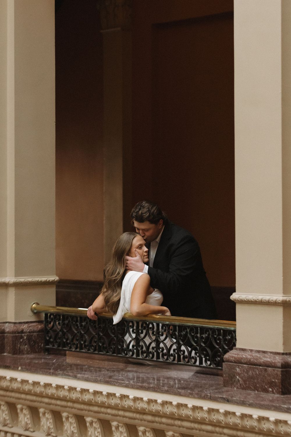 A romantic moment captured on an ornate balcony with decorative railings and classical architecture.