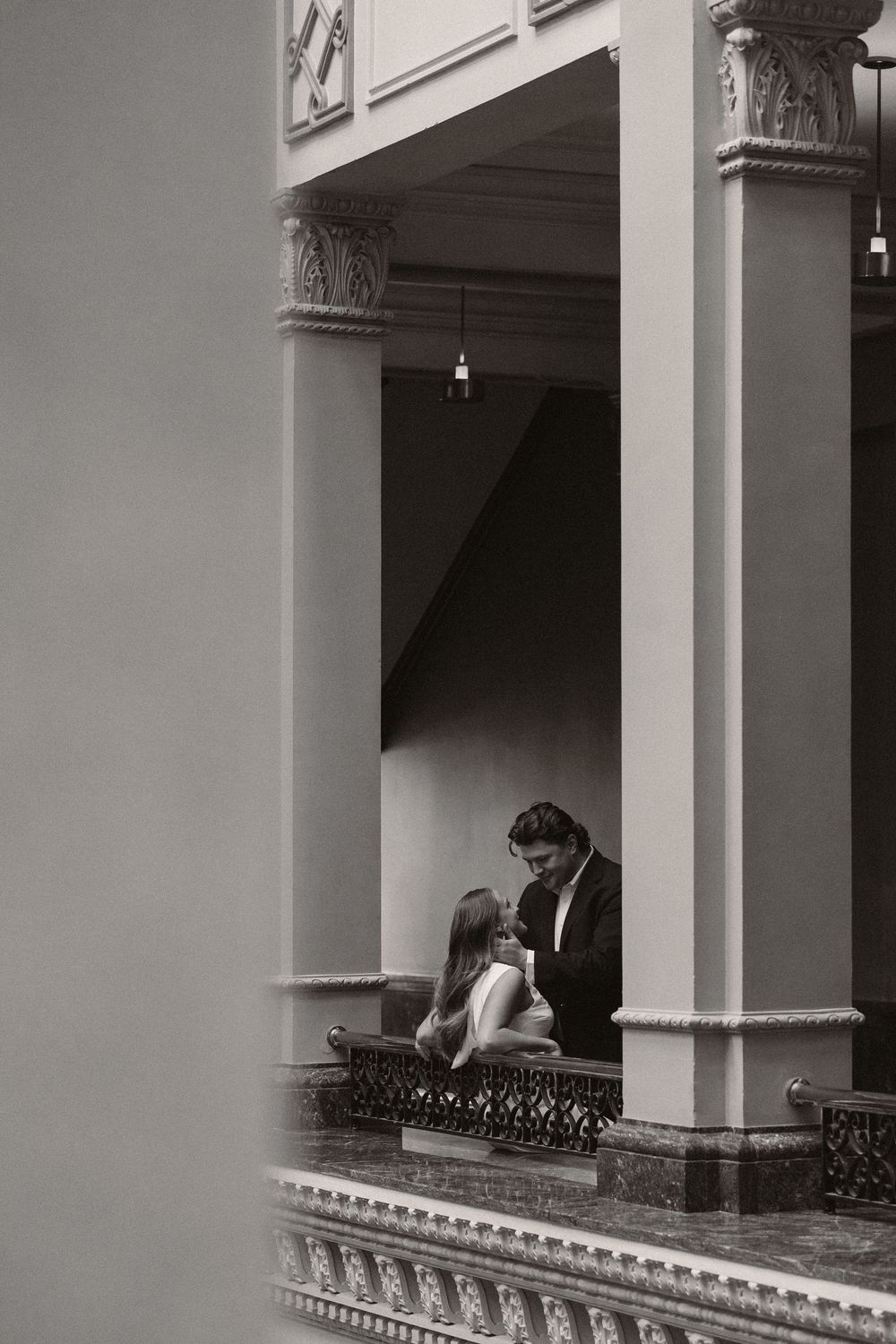 A romantic black and white photograph showing a couple sharing an intimate moment under ornate architectural columns.