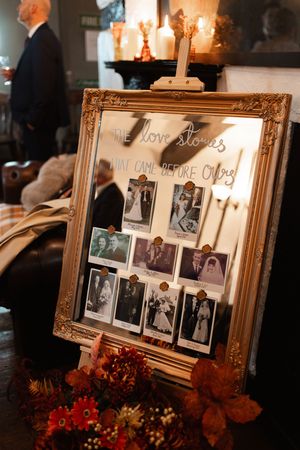 Vintage photographs displayed in an ornate gold frame with autumn flowers and candlelight creating a memorial atmosphere.