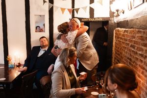 Wedding guests gather in a rustic brick-walled venue with festive bunting decorations hanging overhead.