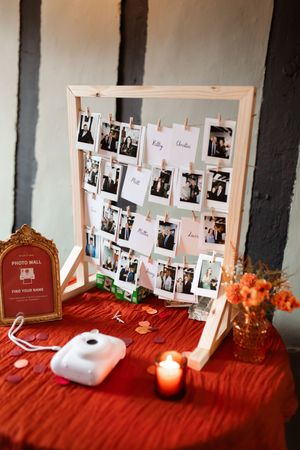 A wedding photo display table with polaroid pictures arranged on red fabric and decorative frames.