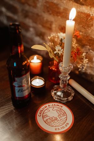 Candlelit table decor with glass holders, beer bottles and a circular coaster with red design.