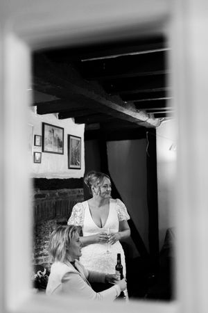 Black and white photograph showing guests mingling at a wedding reception in an intimate indoor setting.