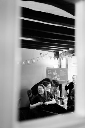 A series of black and white photos showing candid moments through a window frame at what appears to be a social gathering.