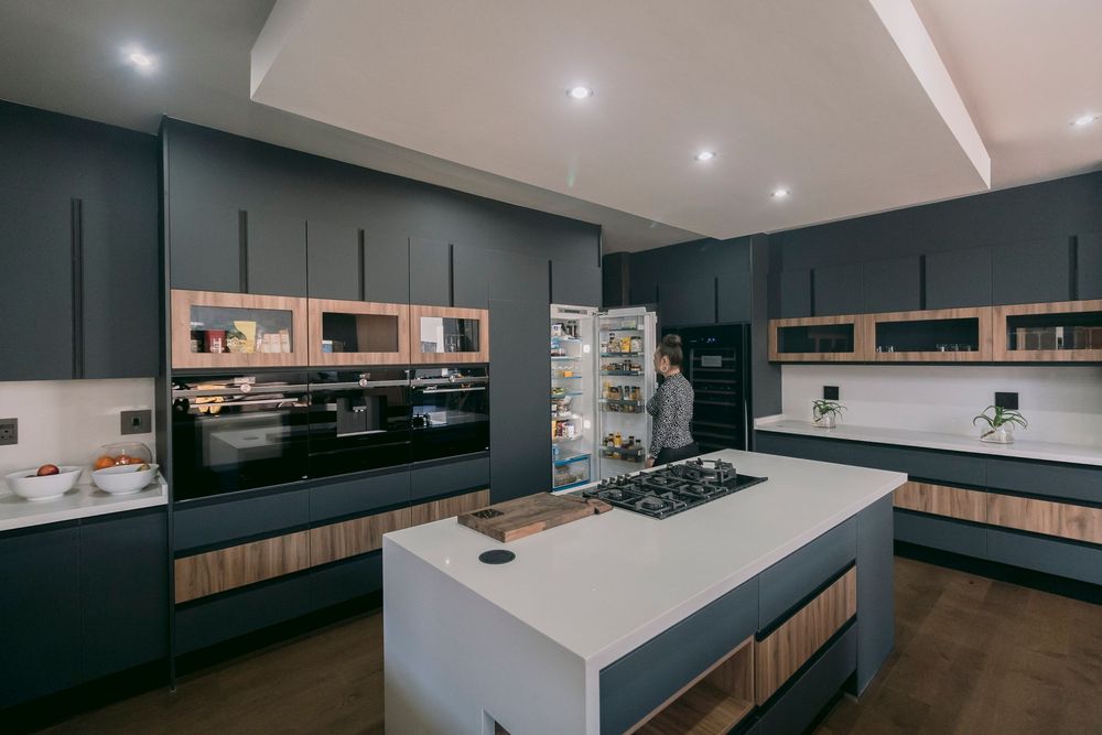 Spacious dark navy kitchen with large white island, built-in appliances, and open shelving with wood accents.