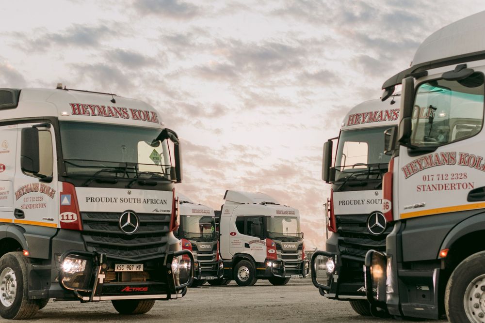 Fleet of Heymans Kole Mercedes-Benz trucks parked under dramatic cloudy sky at dusk.