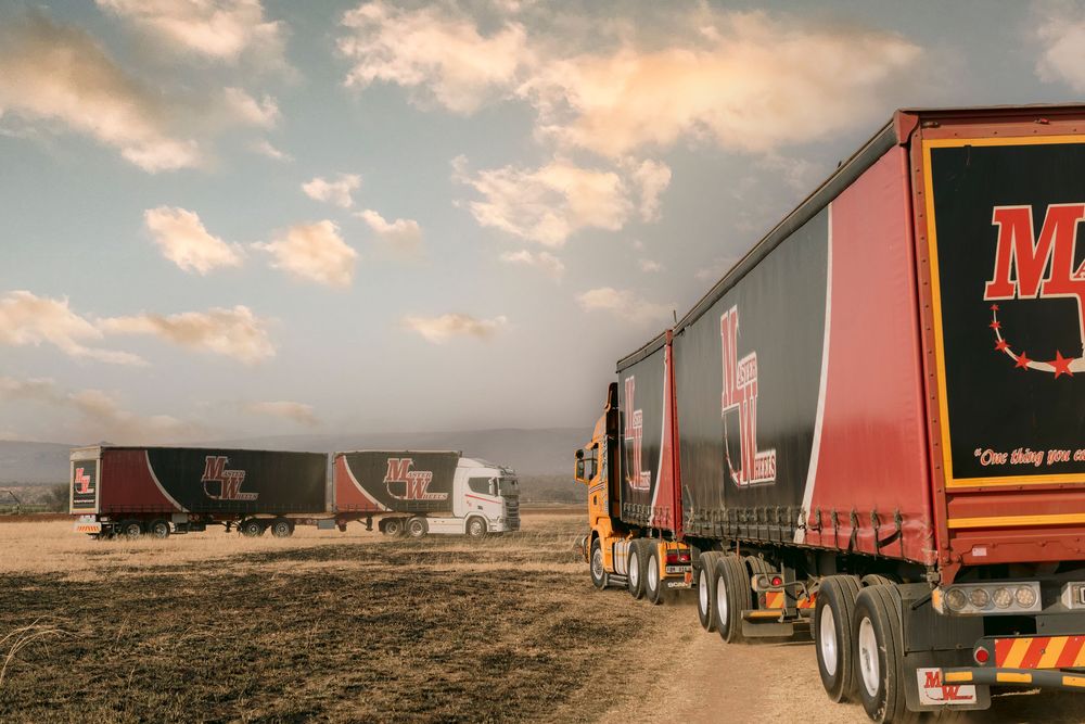 Three red and black branded semi-trucks parked on a dusty road under a dramatic cloudy sky.
