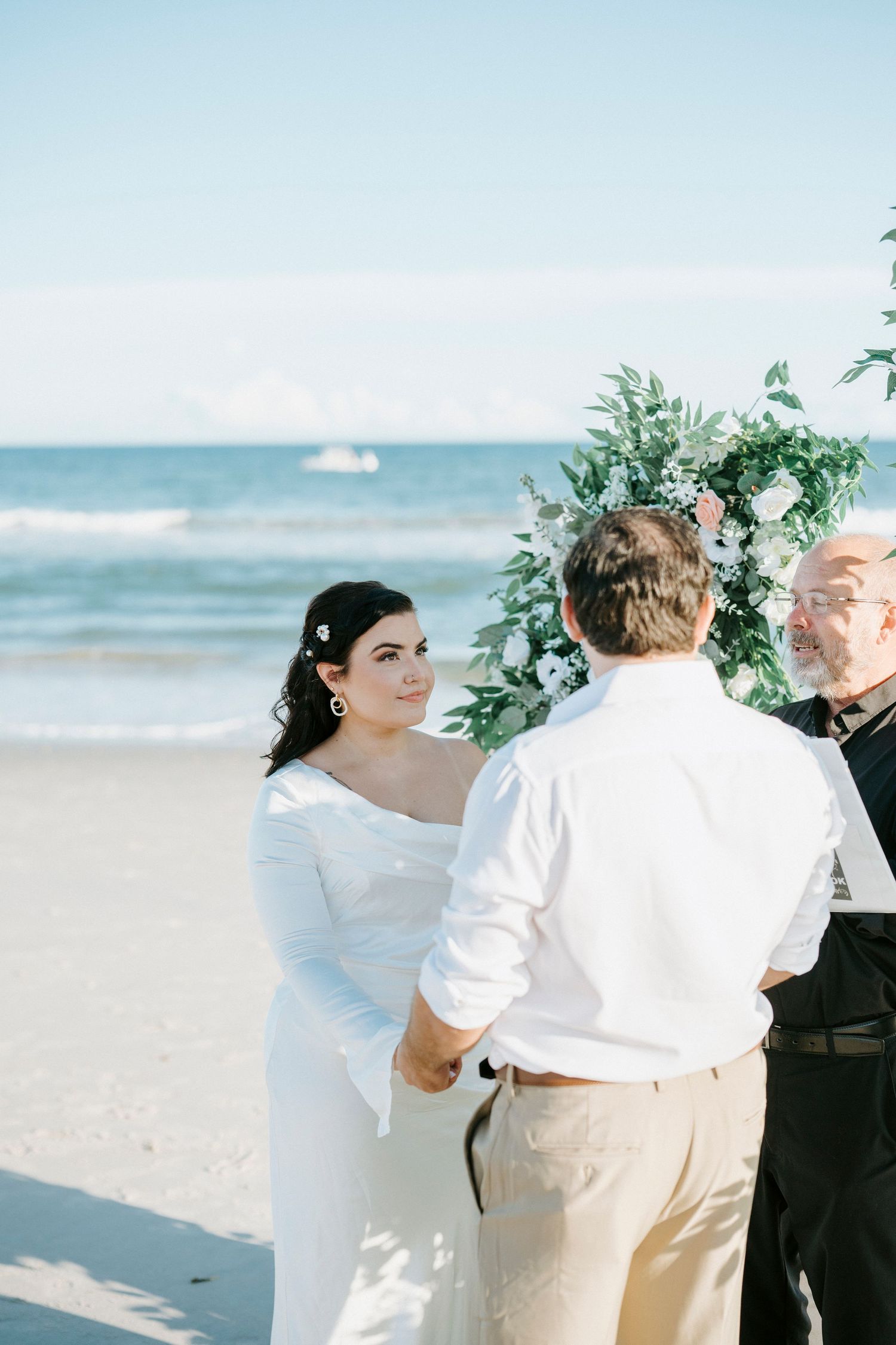 A wedding ceremony takes place on a sunny beach with gentle waves and blue skies in the background.