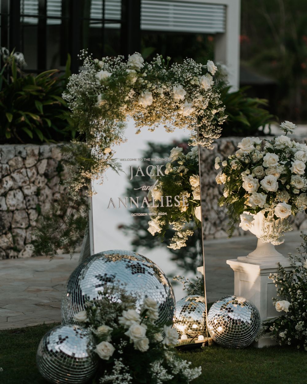 Evening wedding decor features elegant white disco balls adorned with delicate flowers and twinkling lights in an outdoor setting.