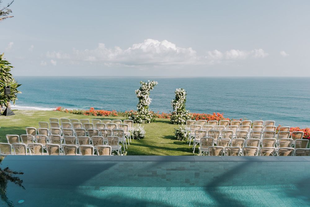 Stunning oceanfront wedding ceremony setup with white chairs and floral arches overlooking an infinity pool and blue sea.
