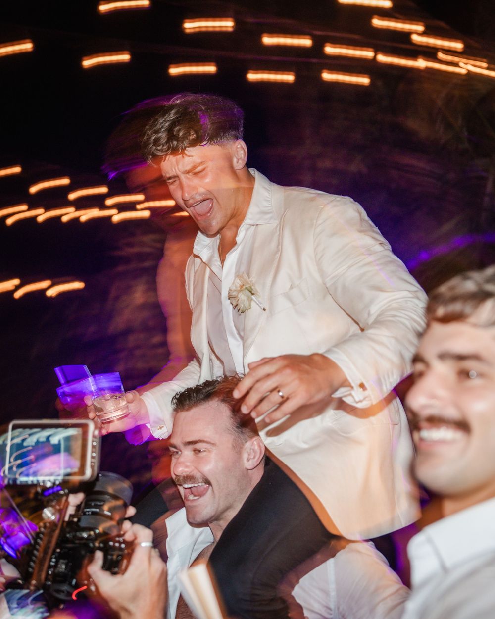 Party guests dance and celebrate on a dimly lit dance floor with glowing orange lights creating a festive atmosphere.