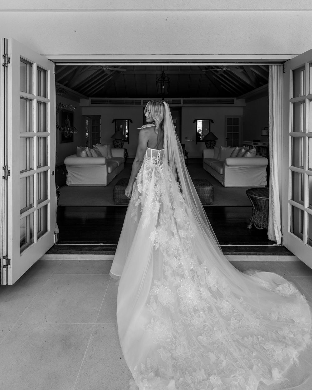 Wedding dress detail showing delicate lace train cascading across white floor in an elegant minimalist room.